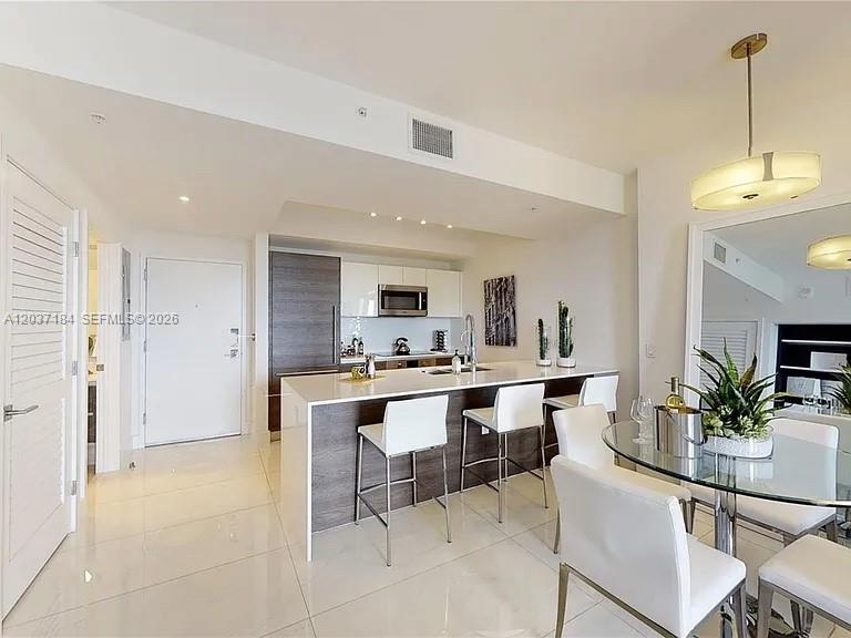 A modern kitchen with a white island, bar stools, and a glass dining table — 301 Altara Ave # 527, Coral Gables FL 33146, CORAL GABLES, FL