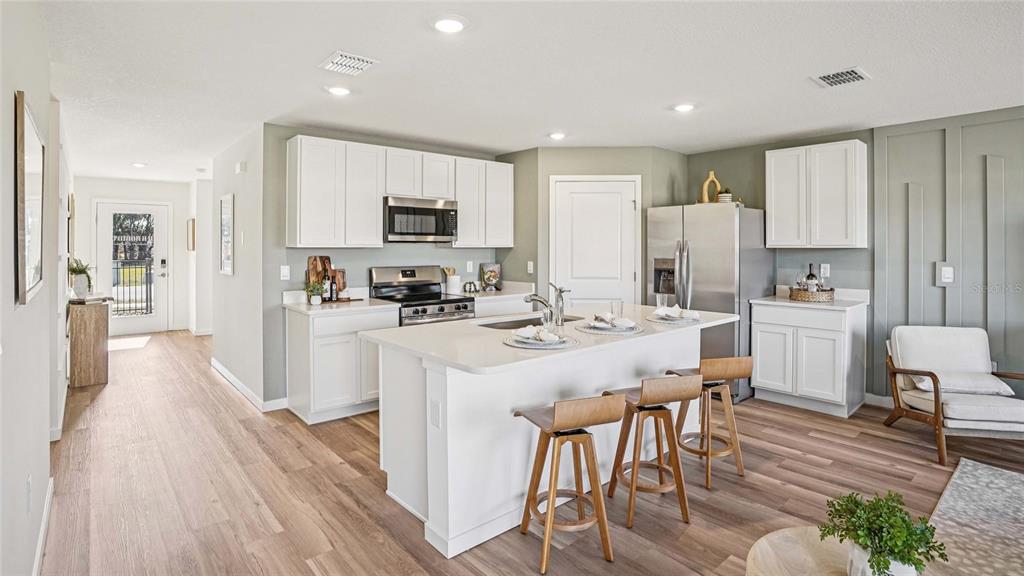 A modern kitchen features white cabinets, a central island with bar stools, and wood flooring — 11036 NW 167TH TERRACE, ALACHUA, FL