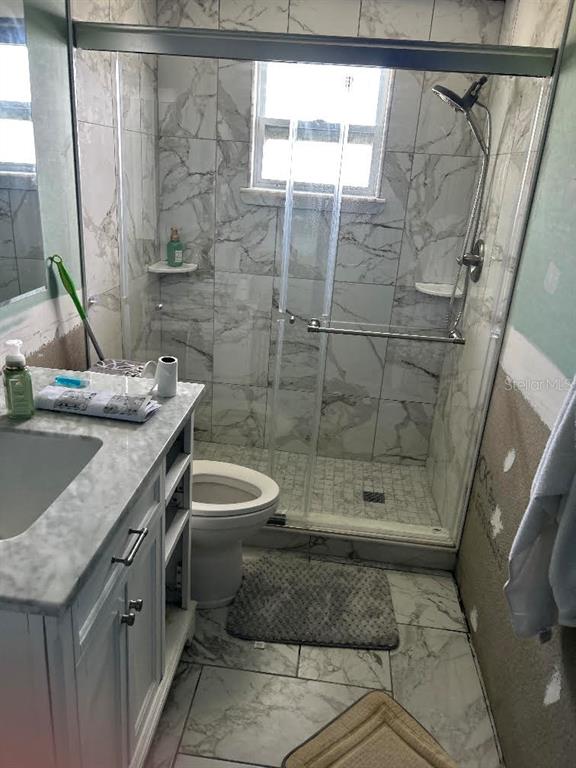 A bathroom features a marble-tiled shower, a white vanity, and an unfinished wall — 13725 PLUMOSA AVENUE, HUDSON, FL