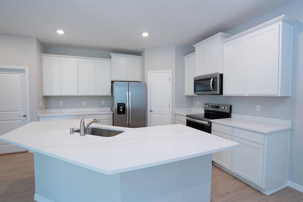 A modern kitchen features white cabinets, stainless steel appliances, and a large white island — 4010 WESTWOOD FIELDS LOOP, PLANT CITY, FL