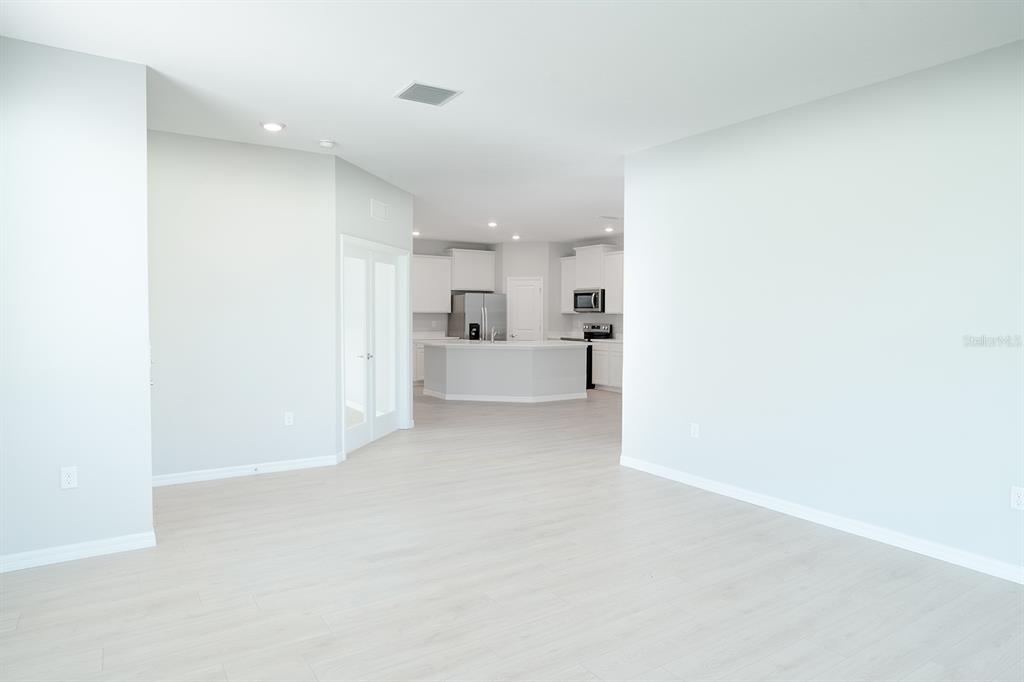 An open-concept living area with light-colored flooring leads to a kitchen with white cabinets — 4010 WESTWOOD FIELDS LOOP, PLANT CITY, FL