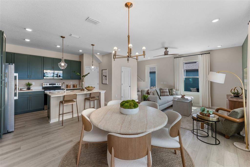 An open-concept kitchen, dining area, and living room featuring dark green cabinets and light flooring — 743 BLISSFUL GARDENS WAY, APOPKA, FL