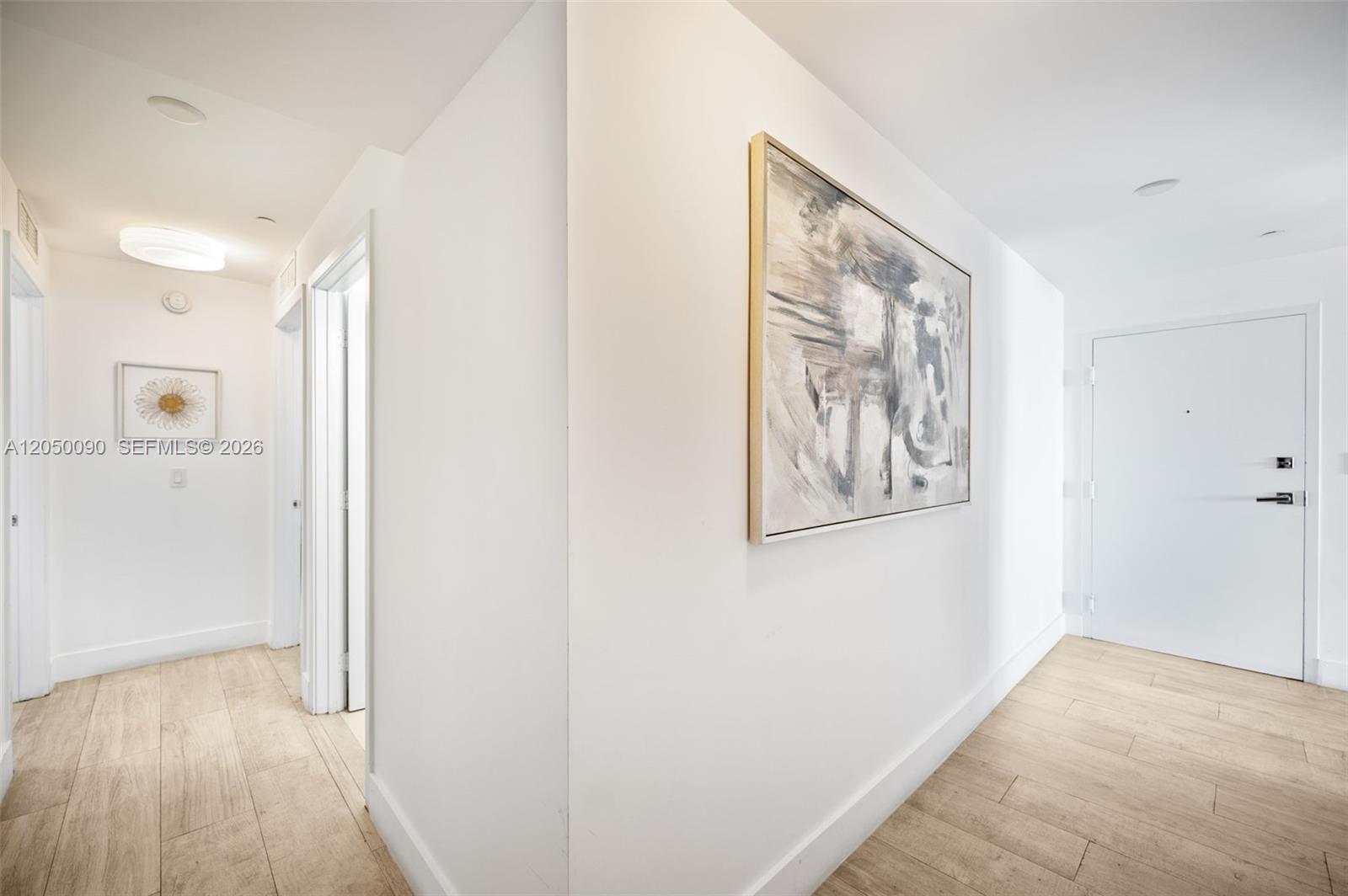 A white hallway features light wood-look tile flooring, two pieces of wall art, and doors — 600 NE 27th St # 1402, Miami FL 33137, MIAMI, FL