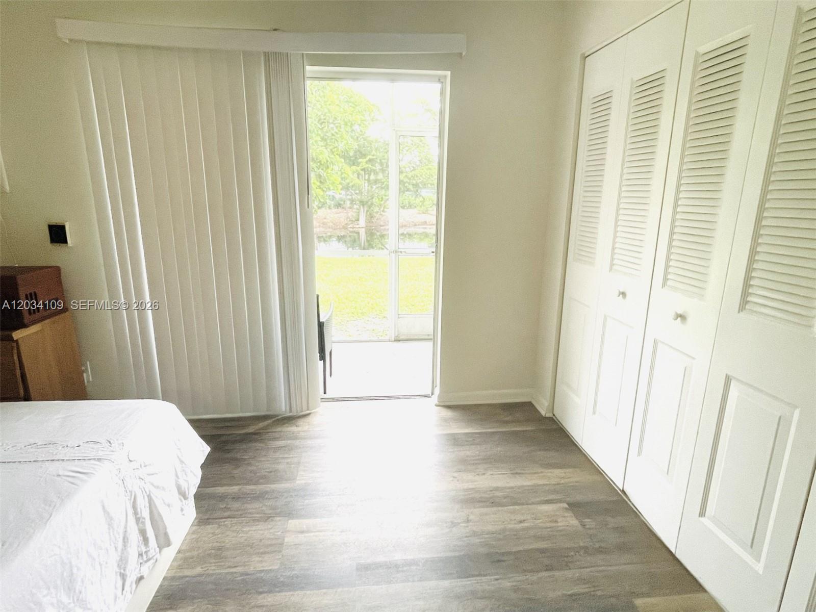 A bedroom features wood-look flooring, white louvered closet doors, and a sliding glass door to a patio — 236 Durham F # 236, Deerfield Beach FL 33442, DEERFIELD BEACH, FL