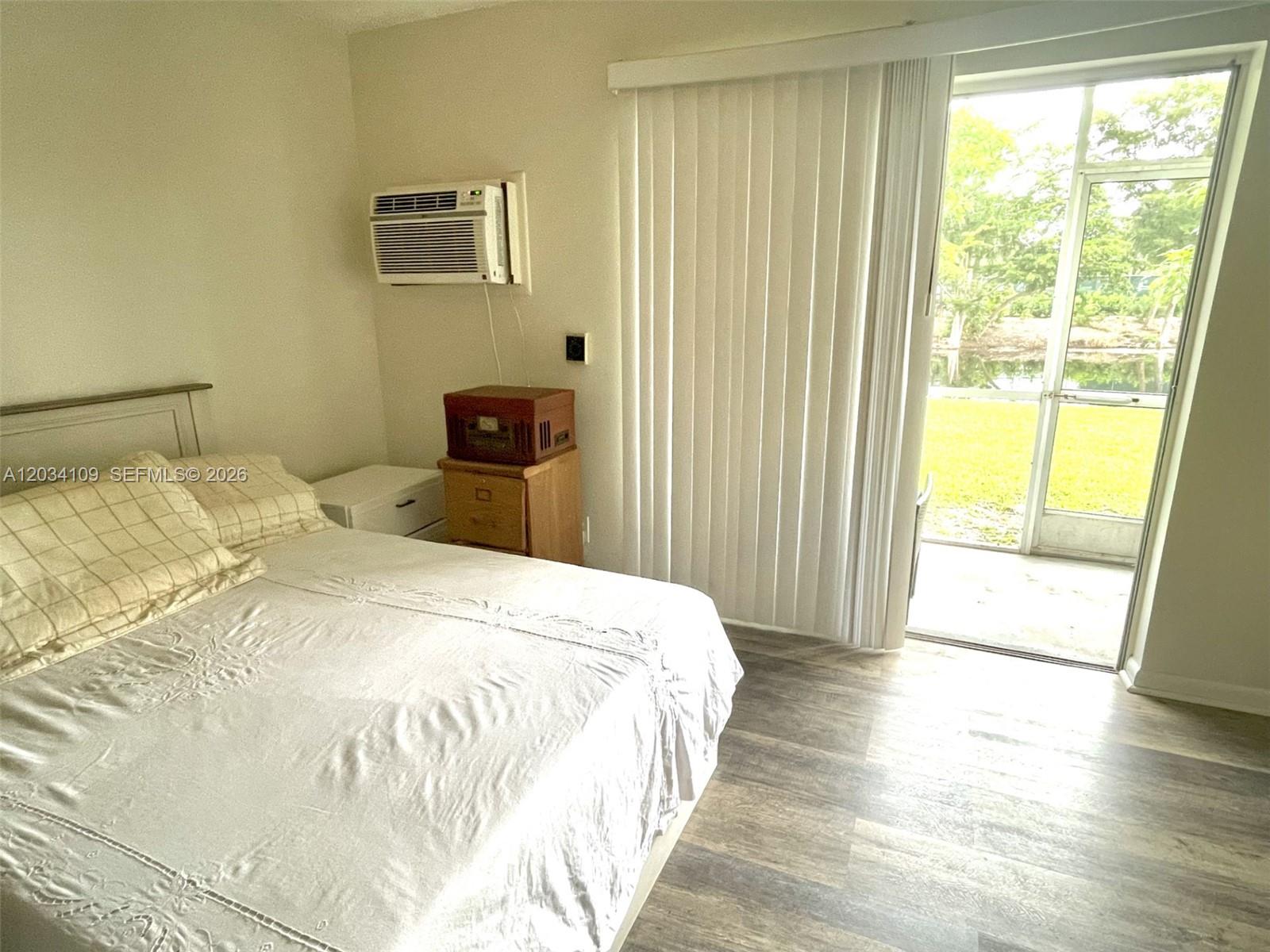 A bedroom features a bed, a window air conditioner, and a sliding door to a patio — 236 Durham F # 236, Deerfield Beach FL 33442, DEERFIELD BEACH, FL