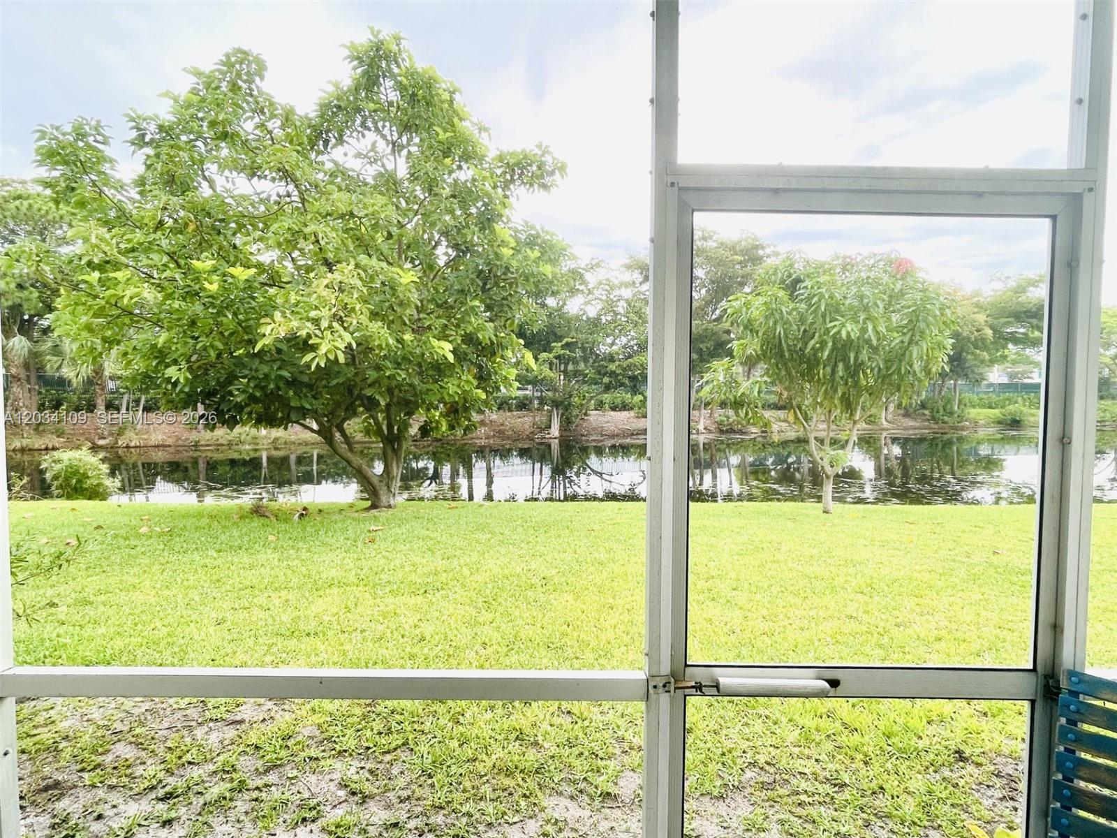 A view of a grassy backyard and a pond seen through a screened-in porch — 236 Durham F # 236, Deerfield Beach FL 33442, DEERFIELD BEACH, FL
