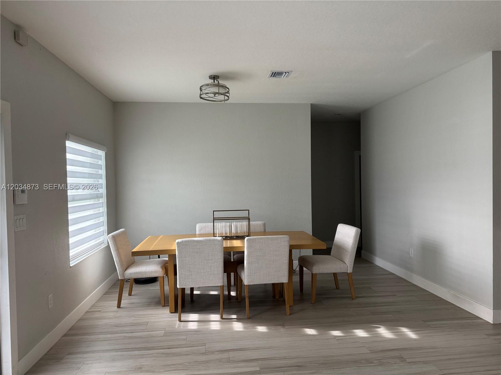 A dining room features a wooden table, six upholstered chairs, and light-colored wood-look flooring — 21483 SW 132nd Pl, Miami FL 33177, MIAMI, FL
