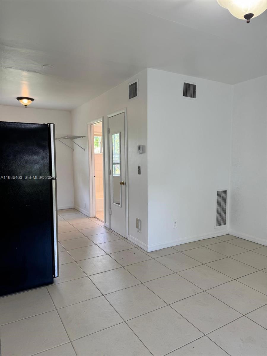 A tiled room features a black refrigerator, a white door, and wall-mounted air vents — 680 NE 88th Ter # 11, Miami FL 33138, MIAMI, FL