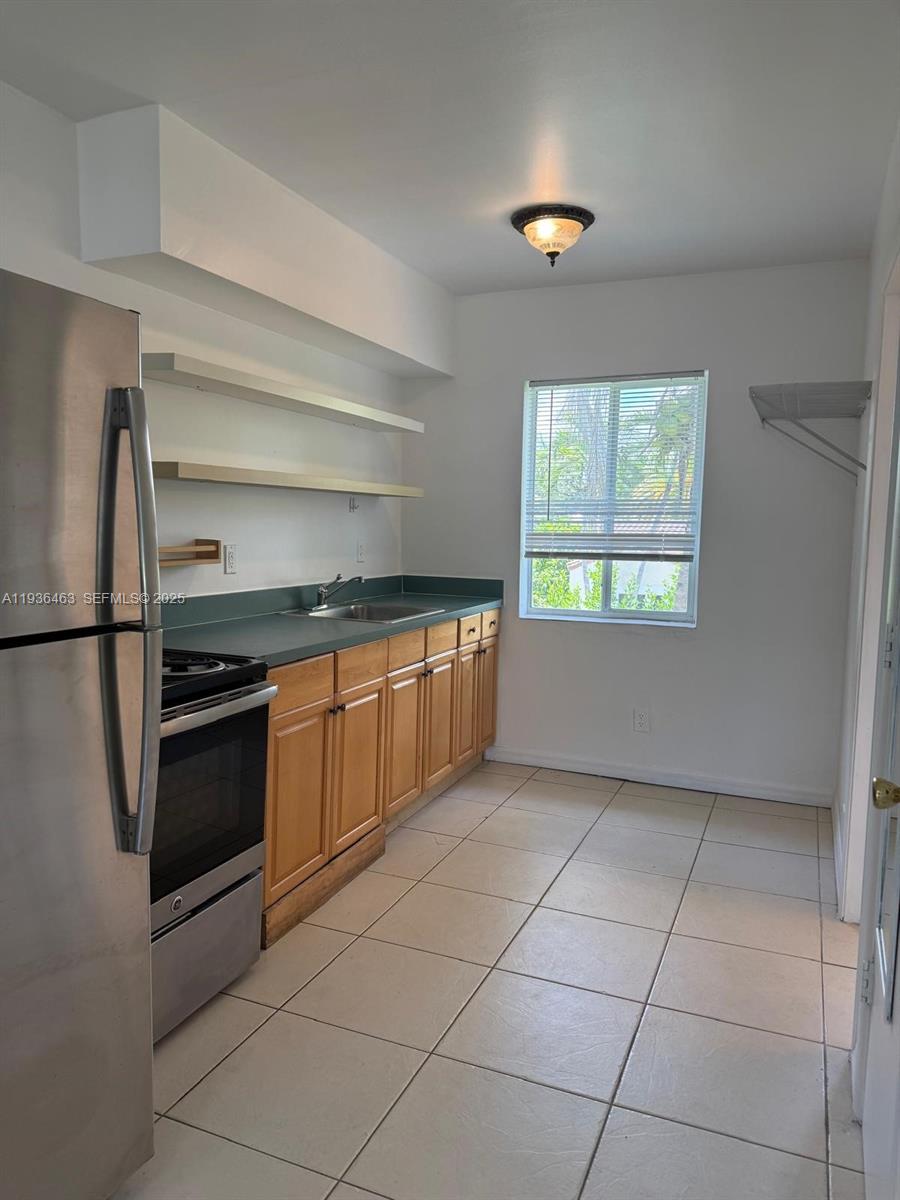 A kitchen features stainless steel appliances, light wood cabinets, green countertops, and tile flooring — 680 NE 88th Ter # 11, Miami FL 33138, MIAMI, FL