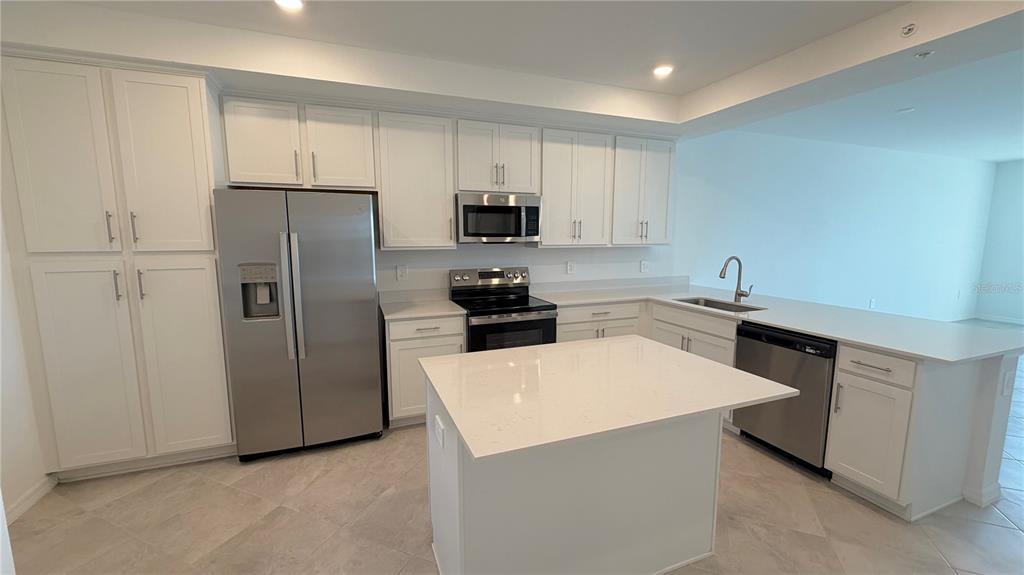 A kitchen with white cabinets, stainless steel appliances, a center island, and light-colored tile flooring — 19116 SCALLOP LOOP UNIT 104, LAKEWOOD RANCH, FL