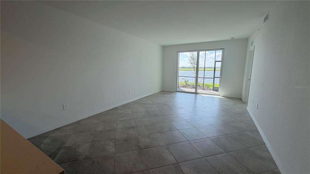 An empty room with light-colored tile flooring and a sliding glass door overlooking a lake — 19116 SCALLOP LOOP UNIT 104, LAKEWOOD RANCH, FL