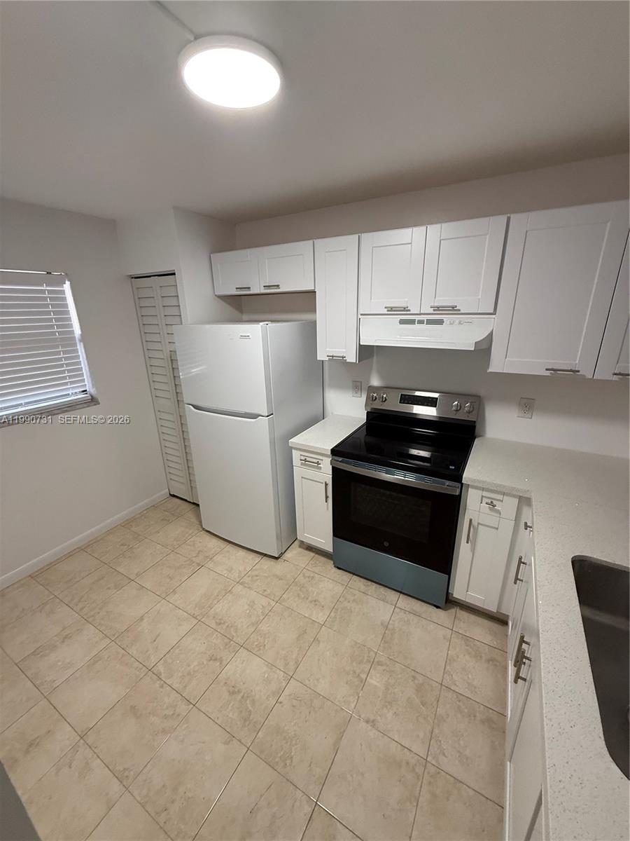 A kitchen features white cabinets, a white refrigerator, a black stove, and tiled flooring — 860 NE 207th Ter # 106, Miami FL 33179, MIAMI, FL