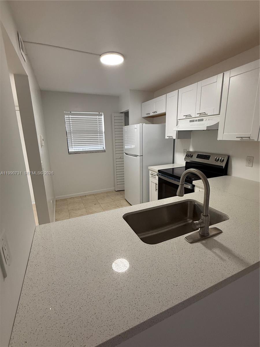 A kitchen features white cabinets, stainless steel appliances, and a light-colored quartz countertop — 860 NE 207th Ter # 106, Miami FL 33179, MIAMI, FL
