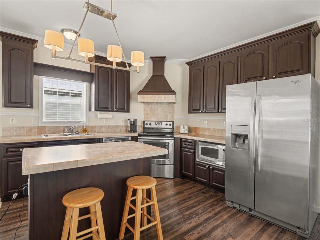 A kitchen features dark wood cabinets, a tiled island with bar stools, and stainless appliances — 312 52ND AVENUE W, BRADENTON, FL