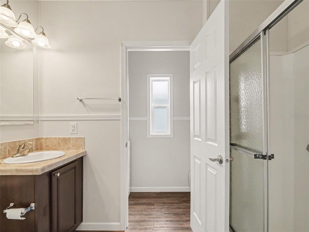 A bathroom features a dark wood vanity, a glass-enclosed shower, and a doorway to a laundry area — 312 52ND AVENUE W, BRADENTON, FL