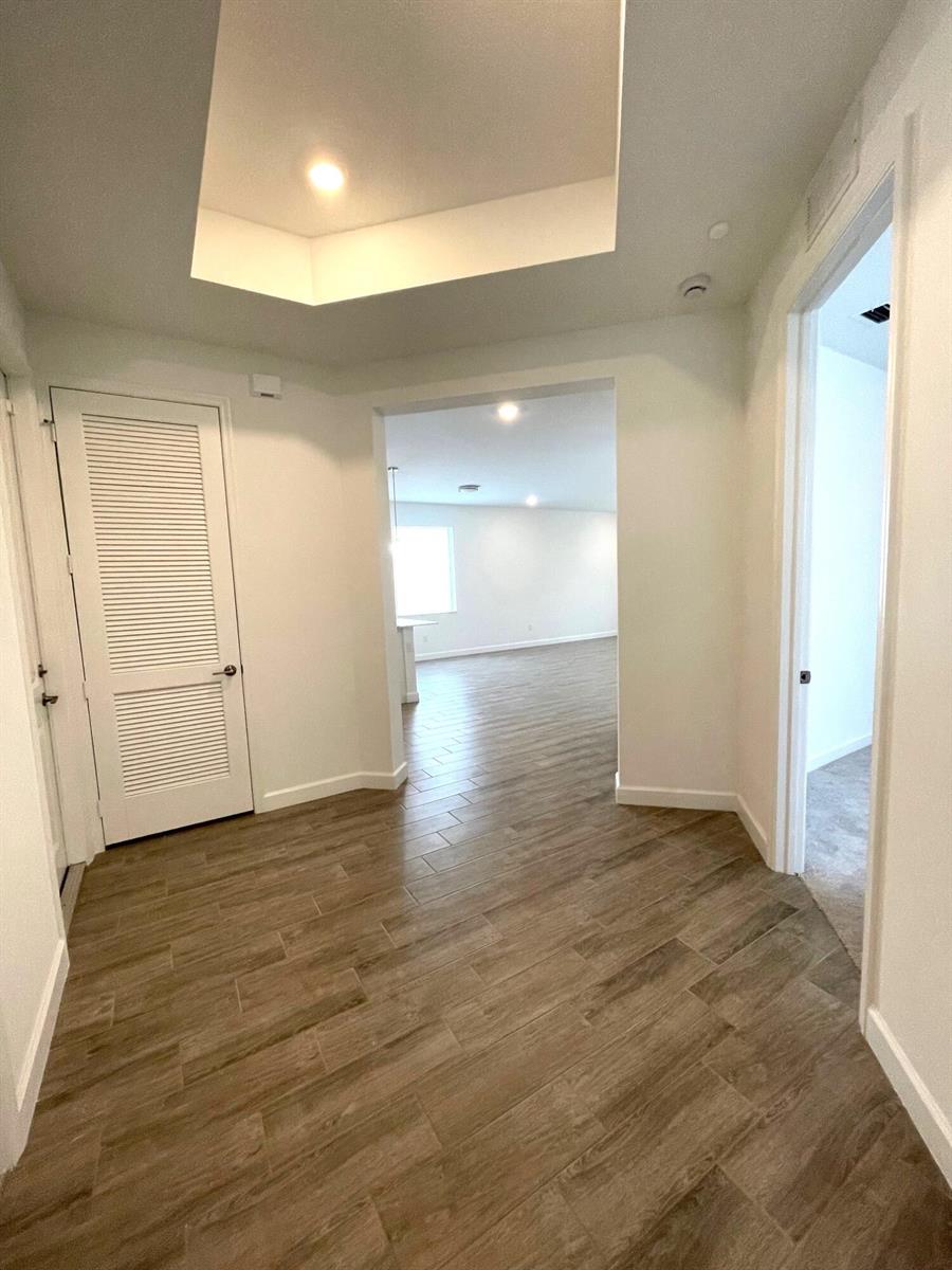 A hallway with wood-look tile flooring leads into an open living space with recessed lighting — 13419 Noble Drive, Delray Beach FL 33484, DELRAY BEACH, FL
