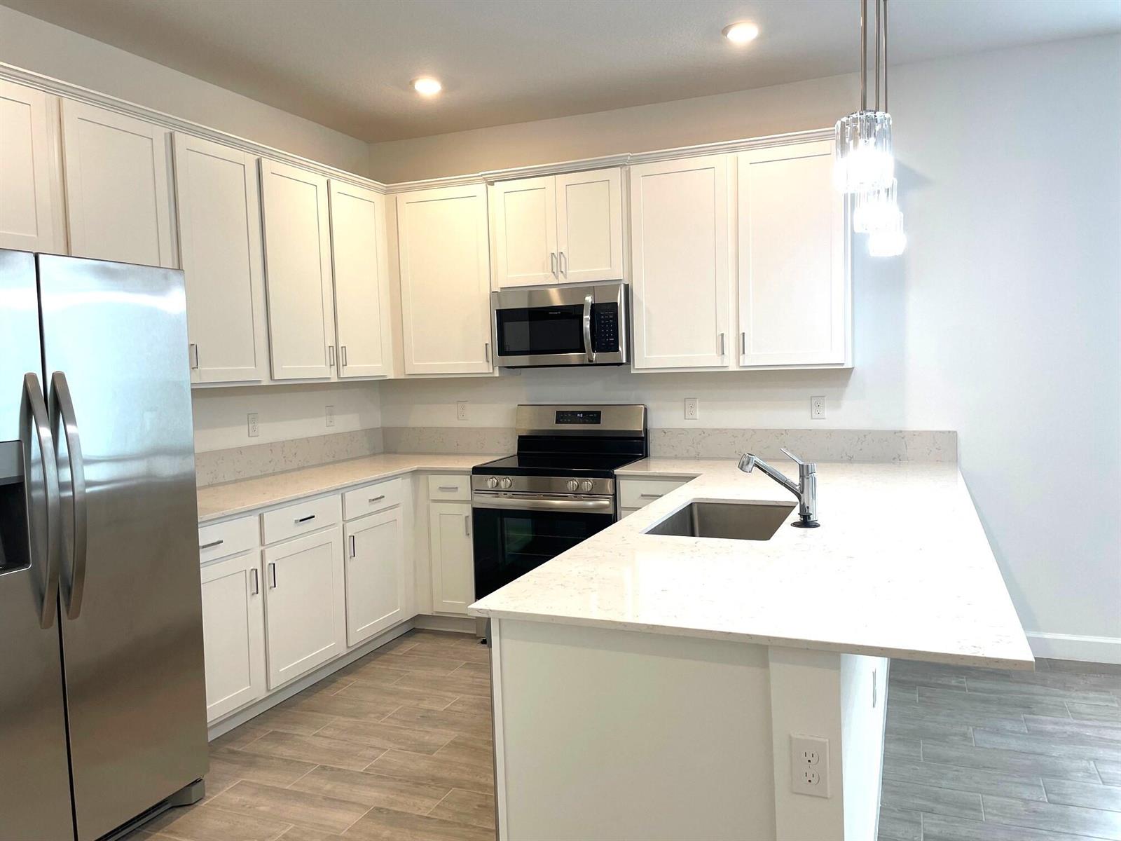 A kitchen features white cabinets, stainless steel appliances, quartz countertops, and light wood-look flooring — 13419 Noble Drive, Delray Beach FL 33484, DELRAY BEACH, FL