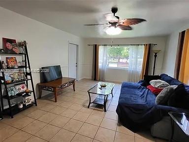 A living room features tile flooring, a blue sofa, a television, and a ceiling fan — 124 NW 6th Ave, Hallandale Beach FL 33009, HALLANDALE BEACH, FL