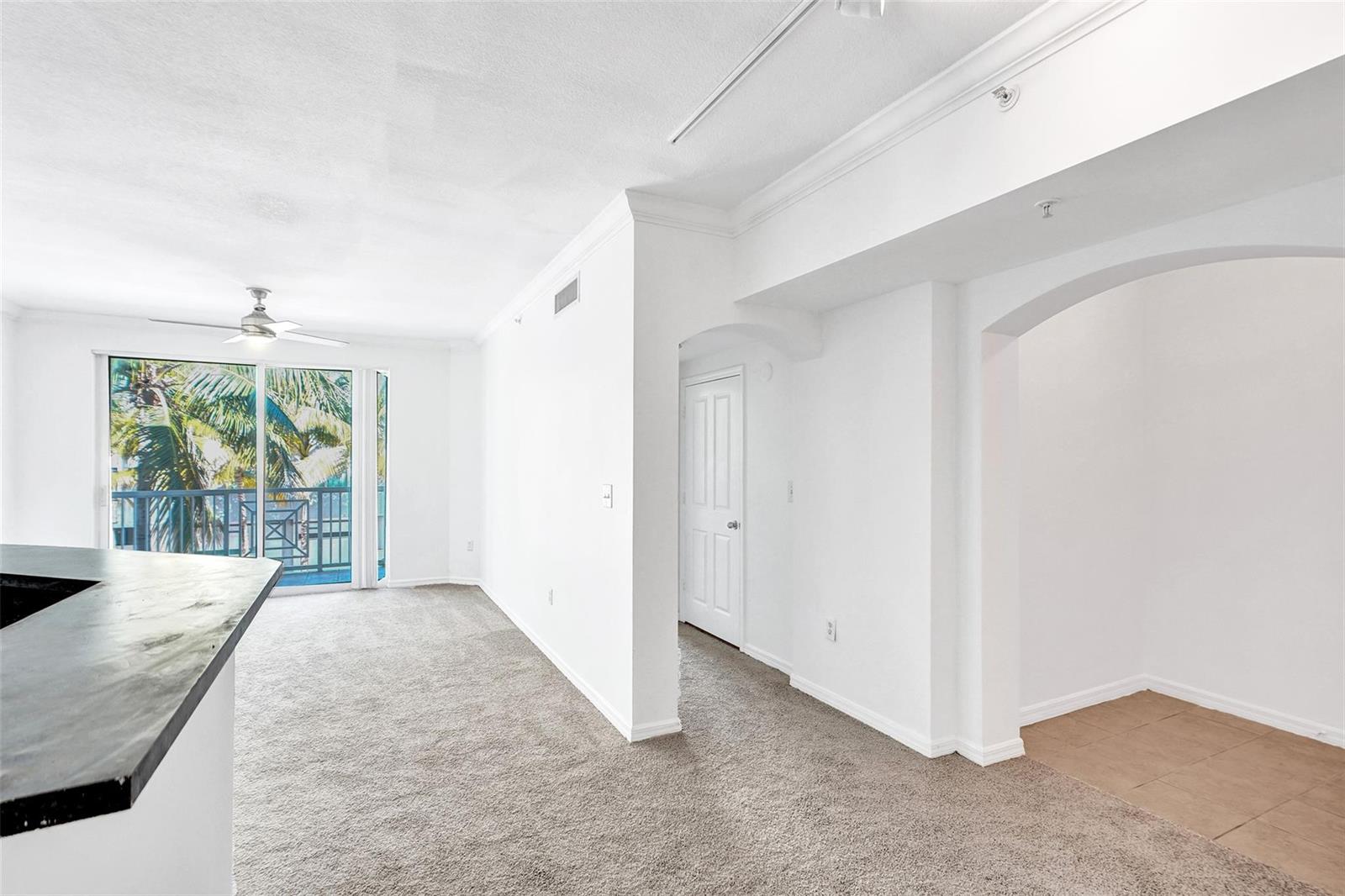 A bright living area features beige carpeting, white walls, and a balcony with palm trees — 9172 Collins Avenue # 302, Surfside FL 33154, SURFSIDE, FL