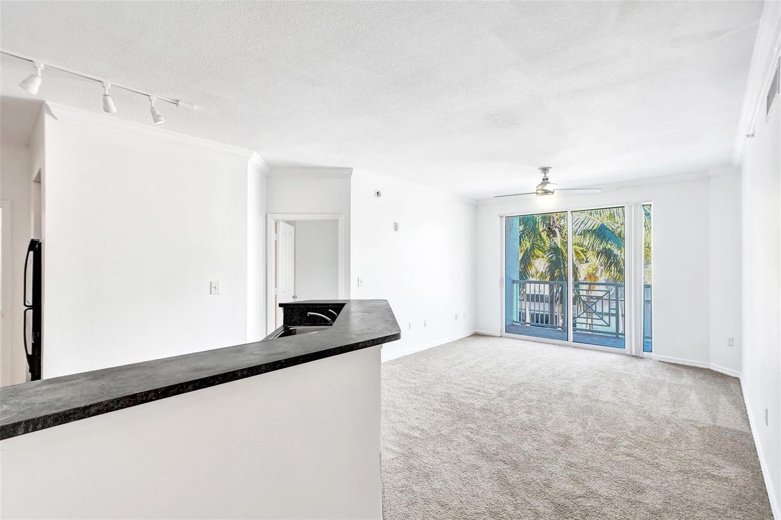 An interior view of a living room with carpeted floors, a breakfast bar, and balcony access — 9172 Collins Avenue # 302, Surfside FL 33154, SURFSIDE, FL
