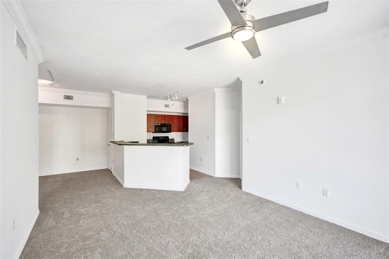 An open-concept living area features gray carpeting, a ceiling fan, and a kitchen breakfast bar — 9172 Collins Avenue # 302, Surfside FL 33154, SURFSIDE, FL