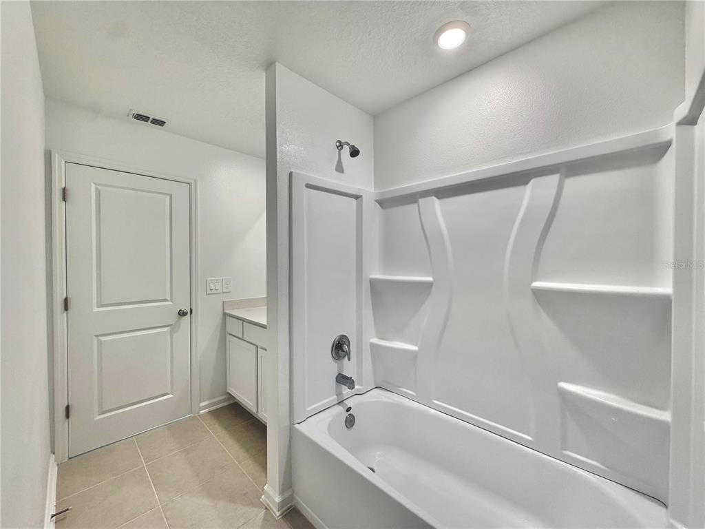 A bathroom features a white bathtub with a shower surround, a vanity, and a door — 3638 HARDMAN DRIVE, LAKE WALES, FL