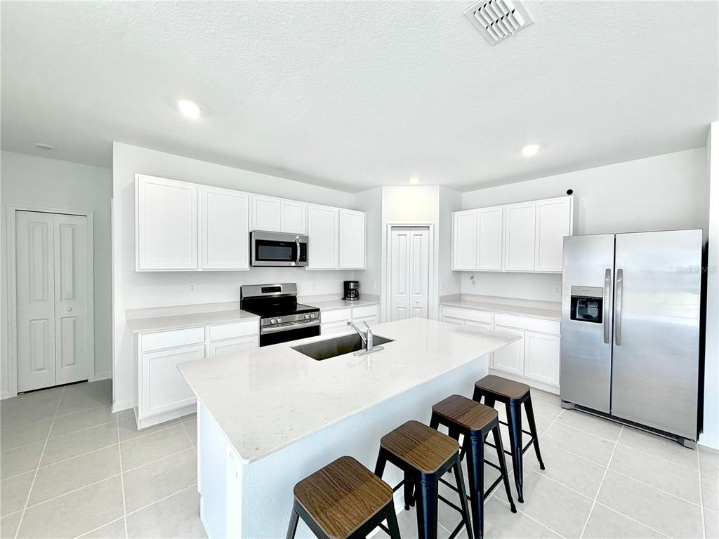 A modern kitchen features white cabinets, stainless steel appliances, a quartz island, and tile flooring — 3638 HARDMAN DRIVE, LAKE WALES, FL