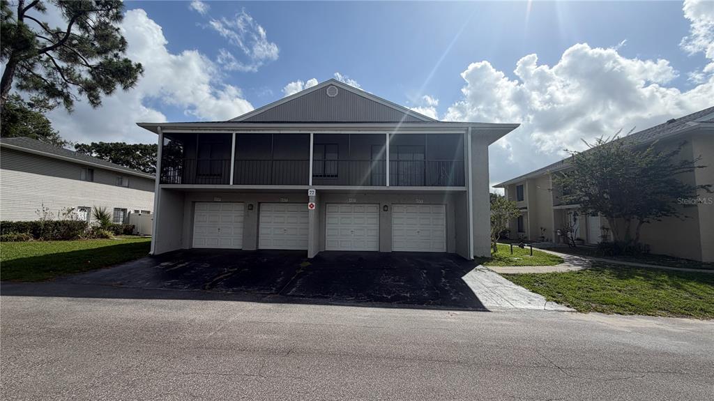 A two-story residential building features four ground-level garage doors and a full-width screened balcony above — 4323 PINEBARK AVENUE UNIT 77-1, ORLANDO, FL