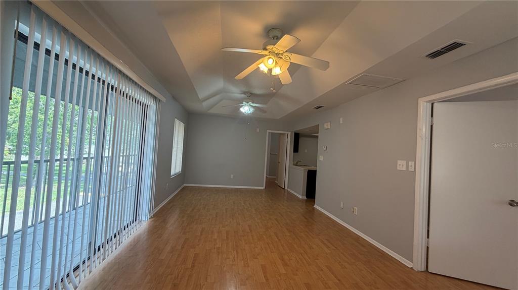 An empty living room features wood-look flooring, a tray ceiling with fans, and vertical blinds — 4323 PINEBARK AVENUE UNIT 77-1, ORLANDO, FL