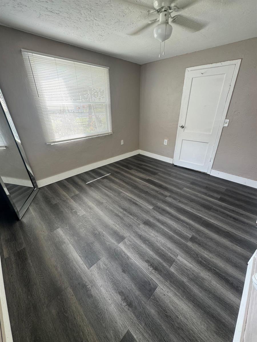 An empty bedroom features gray walls, dark wood-look flooring, a window with blinds, and a ceiling fan — 2467 NW 90th Street, Miami FL 33147, MIAMI, FL