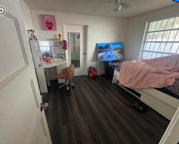 A bedroom features dark wood-look flooring, a white desk, a television, and a twin bed — 2467 NW 90th Street, Miami FL 33147, MIAMI, FL
