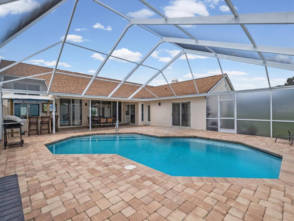 A swimming pool with a screened enclosure sits on a paved patio behind a house — 1302 HENRY AVENUE, SPRING HILL, FL