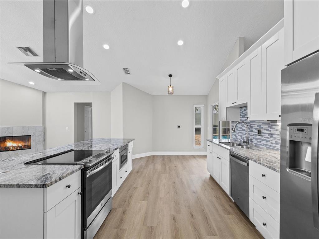 A modern kitchen features white cabinets, granite countertops, stainless steel appliances, and light wood flooring — 1302 HENRY AVENUE, SPRING HILL, FL