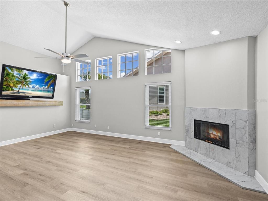 A living room with light wood floors, a vaulted ceiling, a fireplace, and a wall-mounted television — 1302 HENRY AVENUE, SPRING HILL, FL