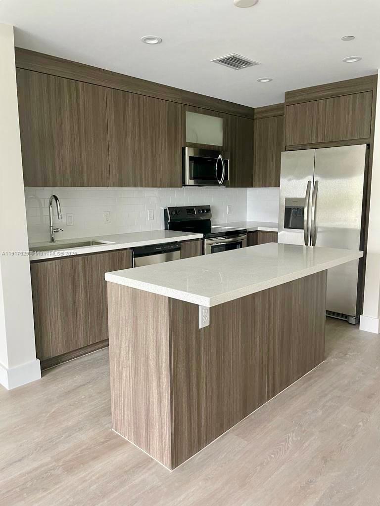 A modern kitchen features wood-grain cabinets, white countertops, stainless steel appliances, and an island — 1938 Jackson St # 403, Hollywood FL 33020, HOLLYWOOD, FL