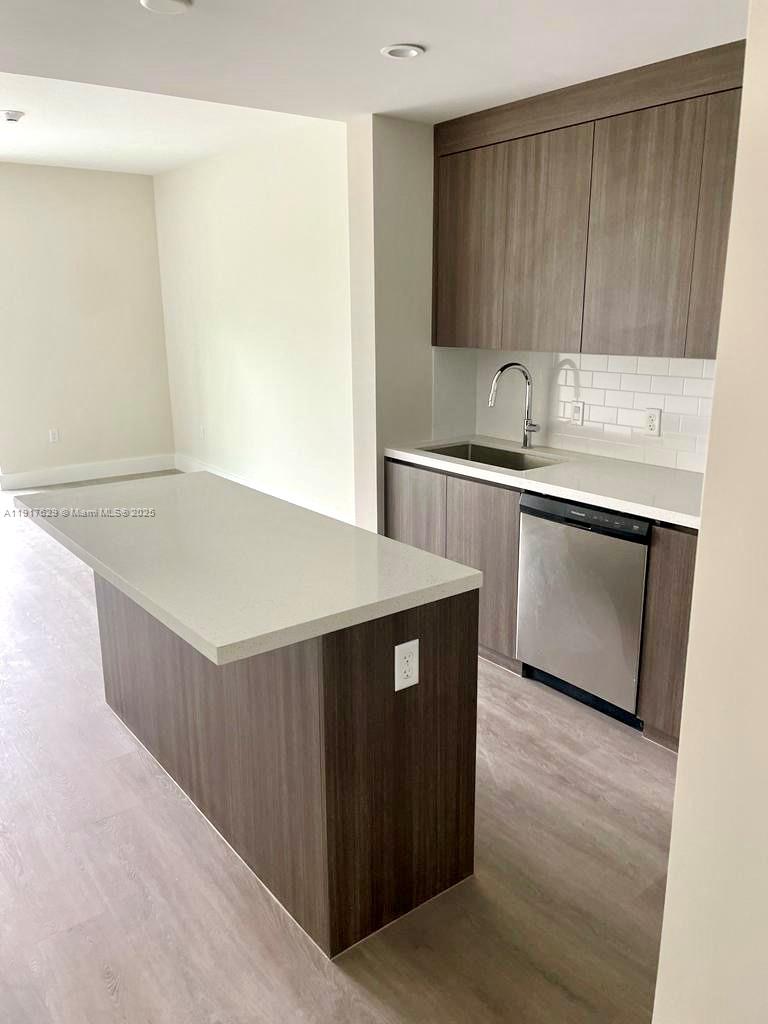 A modern kitchen features wood-toned cabinets, a white quartz island, and stainless steel appliances — 1938 Jackson St # 403, Hollywood FL 33020, HOLLYWOOD, FL