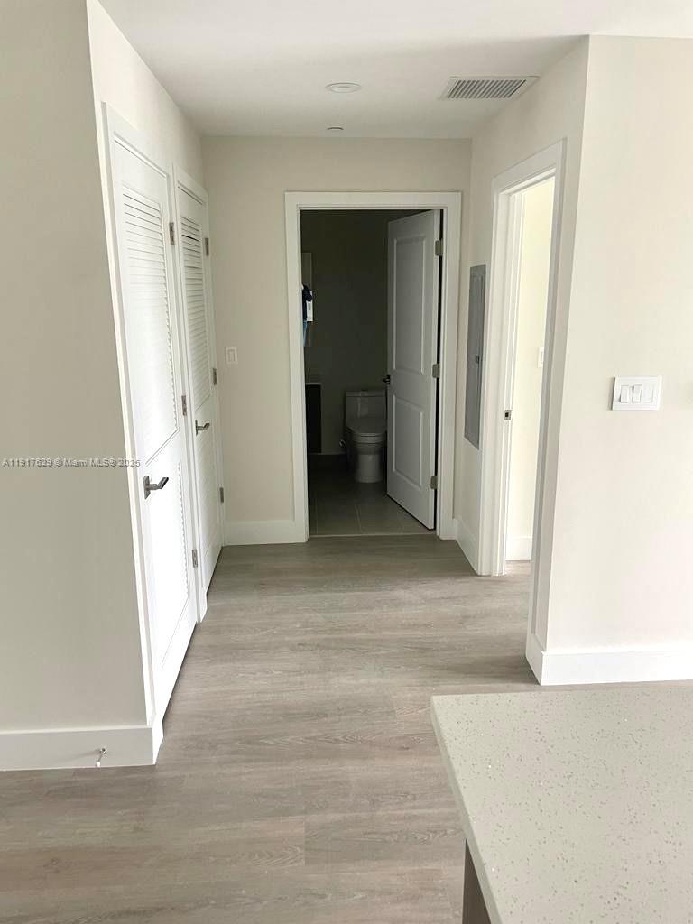 A hallway with light wood-look flooring leads to a bathroom with a white toilet — 1938 Jackson St # 403, Hollywood FL 33020, HOLLYWOOD, FL