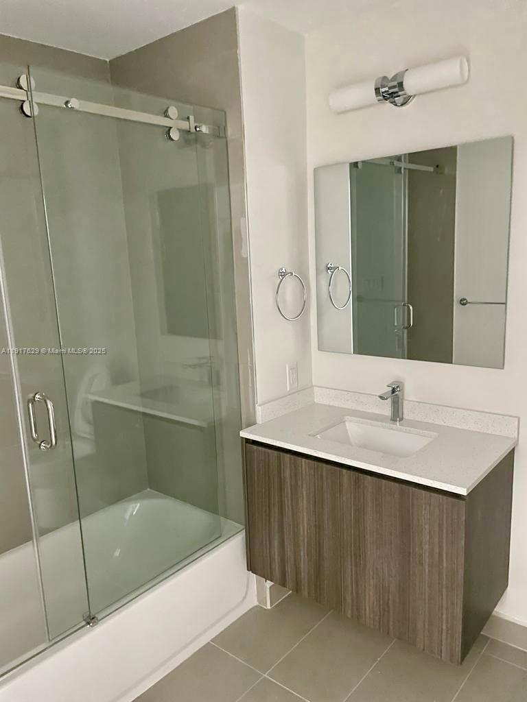A bathroom features a glass-enclosed shower, a wood-toned vanity with a white countertop, and a mirror — 1938 Jackson St # 403, Hollywood FL 33020, HOLLYWOOD, FL