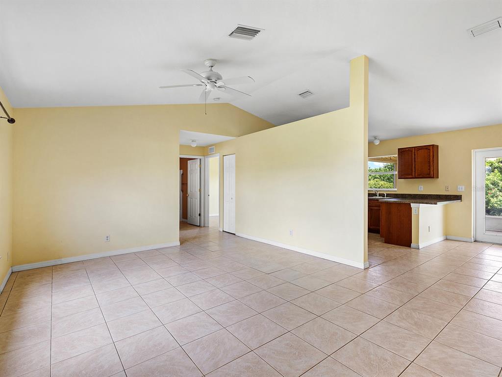 An open-concept living area with tile flooring, yellow walls, and an adjacent kitchen — 12404 WILLMINGTON BOULEVARD, PORT CHARLOTTE, FL