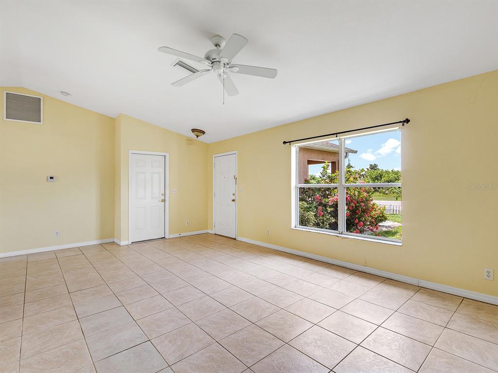 An empty room with yellow walls, tile flooring, a ceiling fan, and a large window — 12404 WILLMINGTON BOULEVARD, PORT CHARLOTTE, FL
