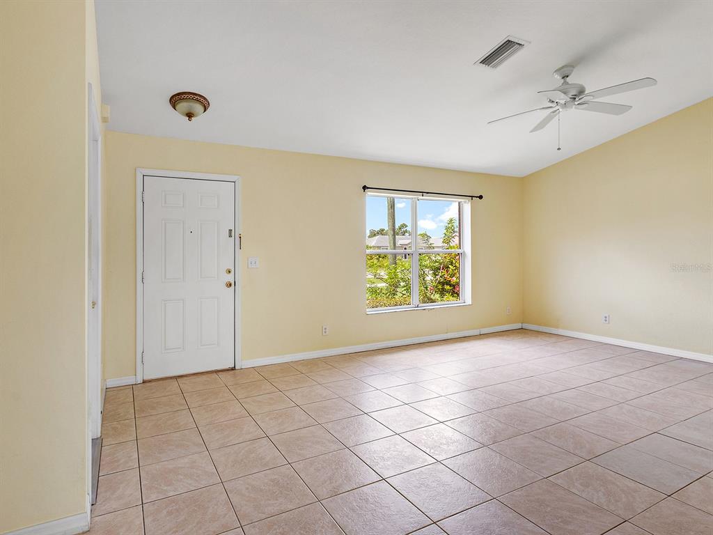 An empty room with light yellow walls, tiled floors, a white door, and a ceiling fan — 12404 WILLMINGTON BOULEVARD, PORT CHARLOTTE, FL