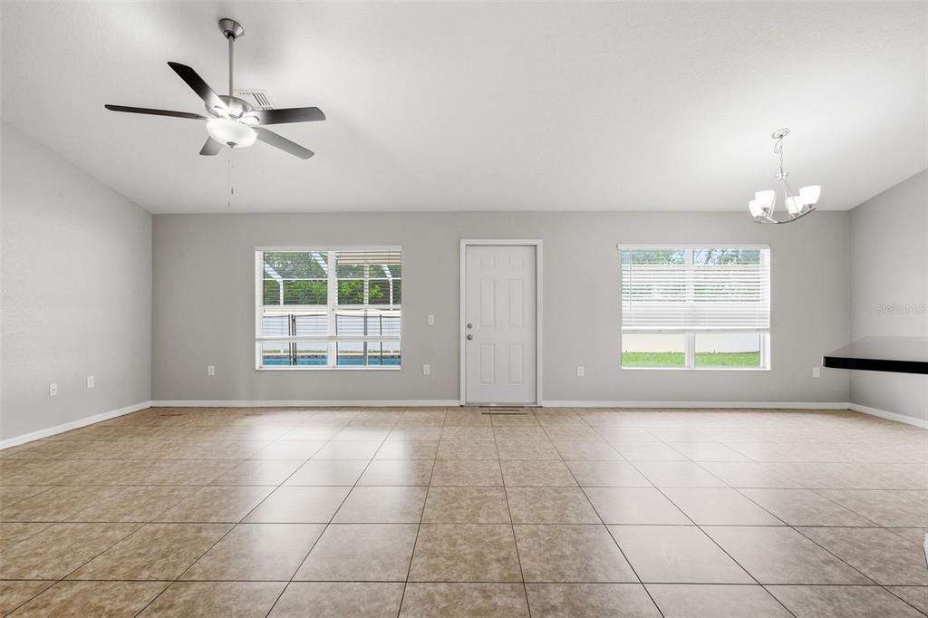 A spacious room with light-colored tile flooring, a ceiling fan, and a central exterior door — 2442 AMBASSADOR AVENUE, SPRING HILL, FL