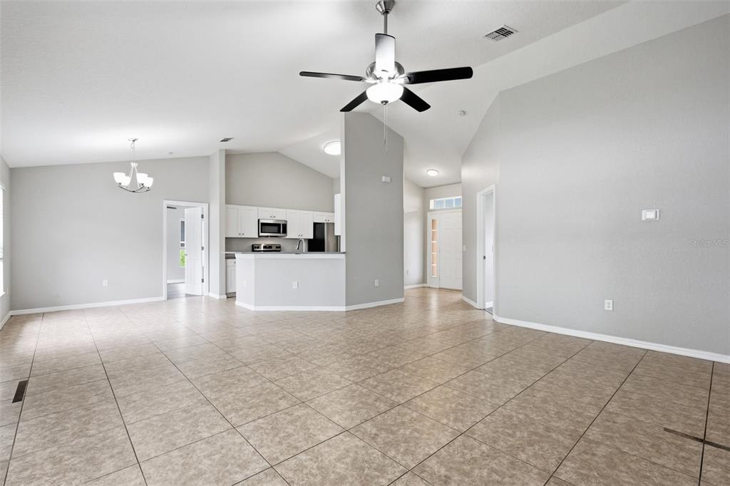 An open-concept living area features light gray walls, tile flooring, and a central kitchen island — 2442 AMBASSADOR AVENUE, SPRING HILL, FL