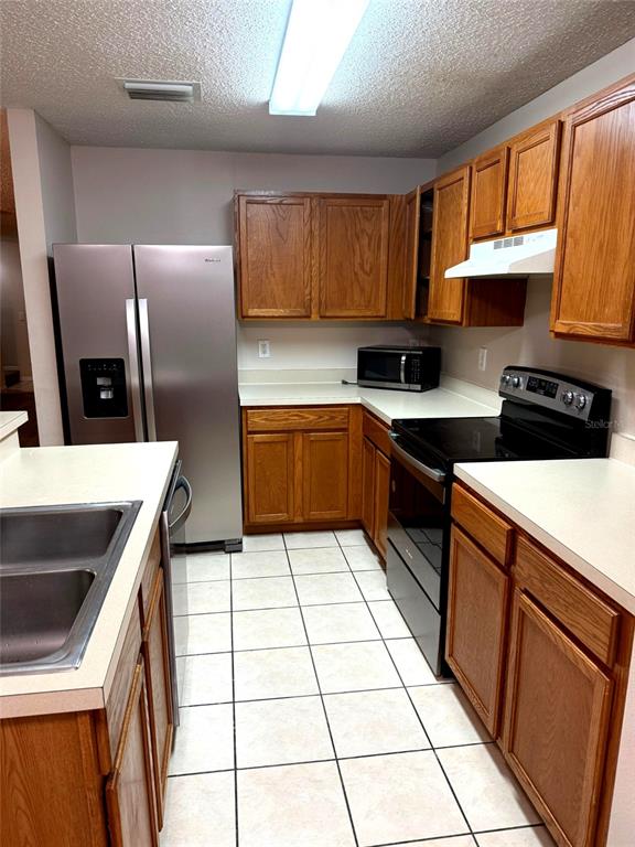 A kitchen features wooden cabinets, stainless steel appliances, white countertops, and a tiled floor — 4104 WINDING RIVER WAY, LAND O LAKES, FL