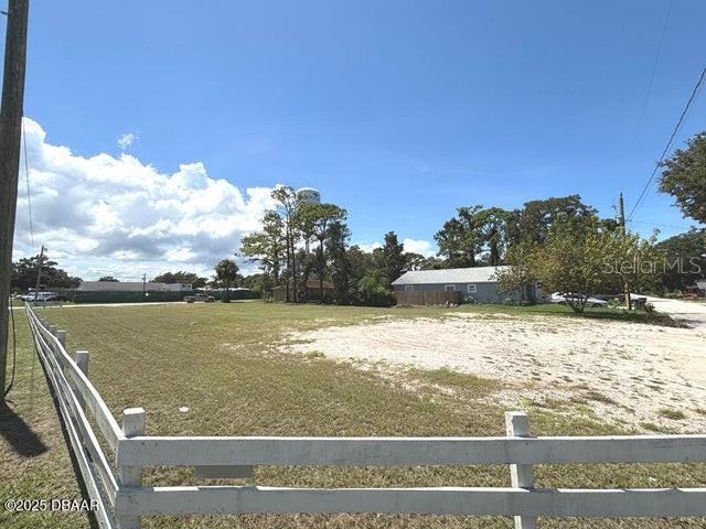 A white fence borders a large, grassy vacant lot with trees and a water tower — 510 LPGA BOULEVARD, DAYTONA BEACH, FL