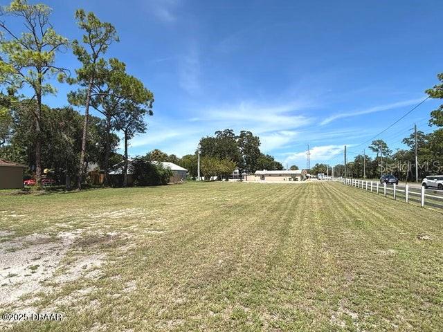 A large, flat, grassy vacant lot is bordered by trees and a white fence — 510 LPGA BOULEVARD, DAYTONA BEACH, FL