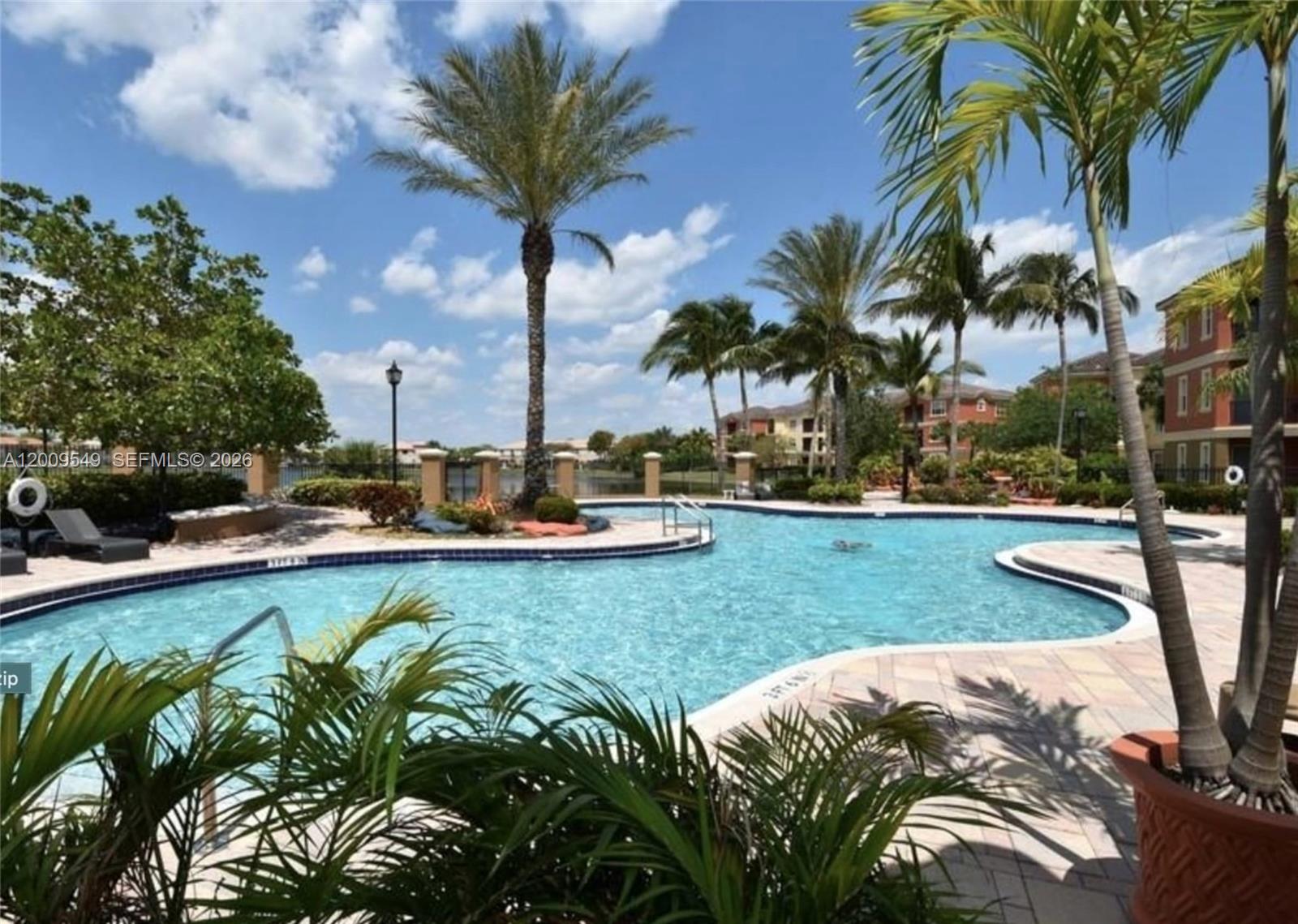 A swimming pool with palm trees and apartment buildings in the background under a blue sky — 4404 SW 160th Ave # 832, Miramar FL 33027, MIRAMAR, FL
