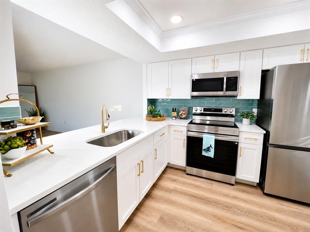 A kitchen features white cabinets, stainless steel appliances, a teal backsplash, and light wood flooring — 3504 BENEVA ROAD UNIT 206, SARASOTA, FL