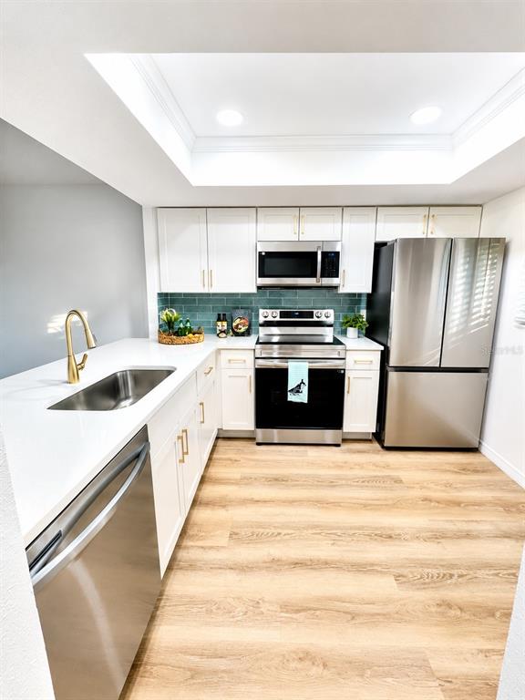 A modern kitchen features white cabinets, stainless steel appliances, and a teal tile backsplash — 3504 BENEVA ROAD UNIT 206, SARASOTA, FL