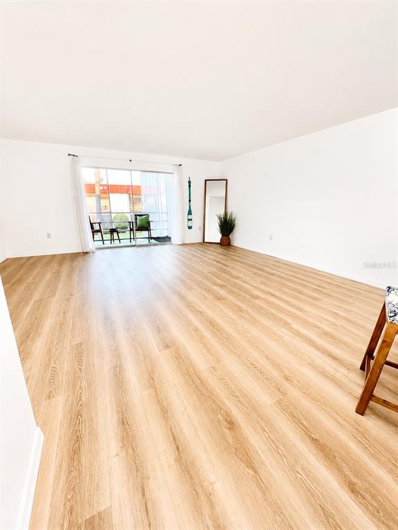 An empty living room features light wood-look flooring, white walls, and a sliding glass door — 3504 BENEVA ROAD UNIT 206, SARASOTA, FL